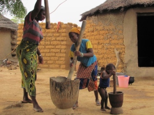 Women manually pounding grain to create meal for cooking.